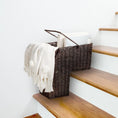 Load image into Gallery viewer, Dark wicker storage stair basket with handles holding books and a folded cream throw on wooden stairs