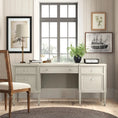 Load image into Gallery viewer, Beige wooden executive desk with multiple drawers and tapered legs in a bright room with framed artwork and plant