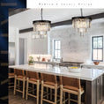 Load image into Gallery viewer, Modern kitchen island with six wooden bar stools and two hanging black crystal chandeliers with gold accents