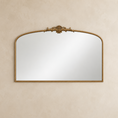 Load image into Gallery viewer, An ornate arched wall mirror with a gold-toned frame and decorative crest at the top, mounted on a textured beige wall.