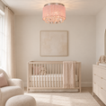 Load image into Gallery viewer, A modern nursery room featuring a light wood crib with a cream knit blanket, a pink crystal drum chandelier, and soft beige walls.