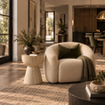 Load image into Gallery viewer, A modern beige boucle armchair with a dark green pillow and a draped throw blanket, set in a beautifully styled contemporary living room with a textured rug, a matching side table, and warm wood cabinetry in the background.