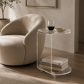Load image into Gallery viewer, A modern acrylic side table with clear glass wheels and a rounded top, styled next to a beige armchair in a minimalist living room setting.