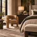 Load image into Gallery viewer, A styled bedroom interior featuring a plush beige velvet accent chair next to a bed with neutral bedding, a wooden nightstand with a lamp, and warm natural light from a window.