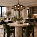 Load image into Gallery viewer, Black globe chandelier with smoked gray glass shades hanging above a marble dining table in a luxury apartment with green velvet chairs and modern decor.