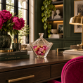 Load image into Gallery viewer, A clear candy dish with a pointed top sits on a dark wood desk in a styled home office. The desk also holds a vase of bright pink peonies, stacked books, a brass desk lamp, and a magenta chair in the foreground.