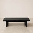 Load image into Gallery viewer, A modern rectangular black coffee table with a slatted top and thick block legs, set against a minimalist beige wall and marble floor.