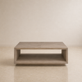 Load image into Gallery viewer, A modern low coffee table with a light gray wood finish and an open lower shelf, set against a minimalist beige wall and floor.