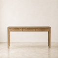 Load image into Gallery viewer, A light natural wood console table with three drawers and slim legs, set against a minimalist beige wall and marble floor.