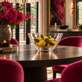 Load image into Gallery viewer, A clear crystal bowl filled with lemons sits on a dark round dining table in a styled dining room with magenta velvet chairs, a large vase of pink flowers, and wall art in the background.
