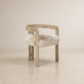 Load image into Gallery viewer, A modern wooden chair with a curved backrest and a fluffy cream sheepskin seat cushion, set against a minimalist beige wall and floor.