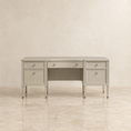 Load image into Gallery viewer, A light gray upholstered writing desk with three drawers, a center drawer, and an open center shelf, shown against a neutral beige textured wall and marble floor.