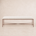 Load image into Gallery viewer, A rectangular upholstered bench with a light beige fabric seat and a dark bronze metal frame featuring crossed lower legs, set against a neutral beige textured background.