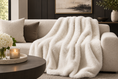 Load image into Gallery viewer, FAUX FUR THROW IVORY on sofa next to pillows and across from a coffee table with a candle on it