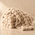 Load image into Gallery viewer, A plush, chunky knit throw blanket in a warm beige color, styled on a polished marble floor against a matching marble wall.