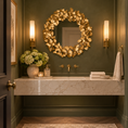 Load image into Gallery viewer, Round gold mirror with sculptural leaf frame above a marble vanity in an elegant powder room with olive green walls and brass sconces.
