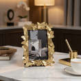 Load image into Gallery viewer, A rectangular picture frame with an ornate border made of metallic gold leaves and butterflies, holding a photograph of a white fireplace and chair scene.