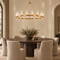 Load image into Gallery viewer, A modern circular chandelier with a gold-toned metal frame and clear glass candle-style bulbs hangs over a round dark wood dining table surrounded by six upholstered dining chairs in a warm, elegant dining room.