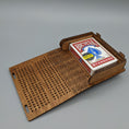 Load image into Gallery viewer, Foldable wooden cribbage board with hole scoring track and compartment holding a standard Bicycle playing card deck on gray background