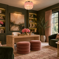 Load image into Gallery viewer, A luxurious home office or study featuring dark green paneled walls, built-in shelves with warm lighting, a large abstract painting, a marble desk, two round dusty rose velvet ottomans, a green velvet sofa, and a pink crystal chandelier.