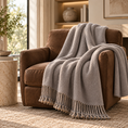 Load image into Gallery viewer, Gray Reversible Mulberry Silk Throw with hand-knotted fringe draped over a brown accent chair in a warm neutral living room.