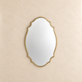 Load image into Gallery viewer, An ornate oval wall mirror with a gold scalloped frame, mounted on a textured beige wall.