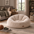 Load image into Gallery viewer, A round, tufted beige fabric bean bag chair sits on a woven rug in a styled bedroom setting with a bed, window, and bookshelves visible in the background.