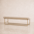 Load image into Gallery viewer, A modern upholstered bench with a light beige fabric seat cushion and a slim gold metal frame, set against a neutral beige textured wall and floor.