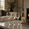 Load image into Gallery viewer, wine glass set on a marble table in a cozy living room setting, with a bottle of Grace Valley White Wine and a book in the background.