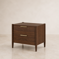 Load image into Gallery viewer, A mid-century modern two-drawer nightstand in dark walnut wood with brass handles, set against a neutral beige wall and floor.