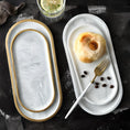 Load image into Gallery viewer, Two House of Effy MINIMALIST OVAL SERVING PLATES: the left one is empty with golden edges, while the right complements a sophisticated tableware setting with a pastry, fork, and coffee beans. An elegant drink garnished with a flower and lemon slice sits adjacent to the trays.
