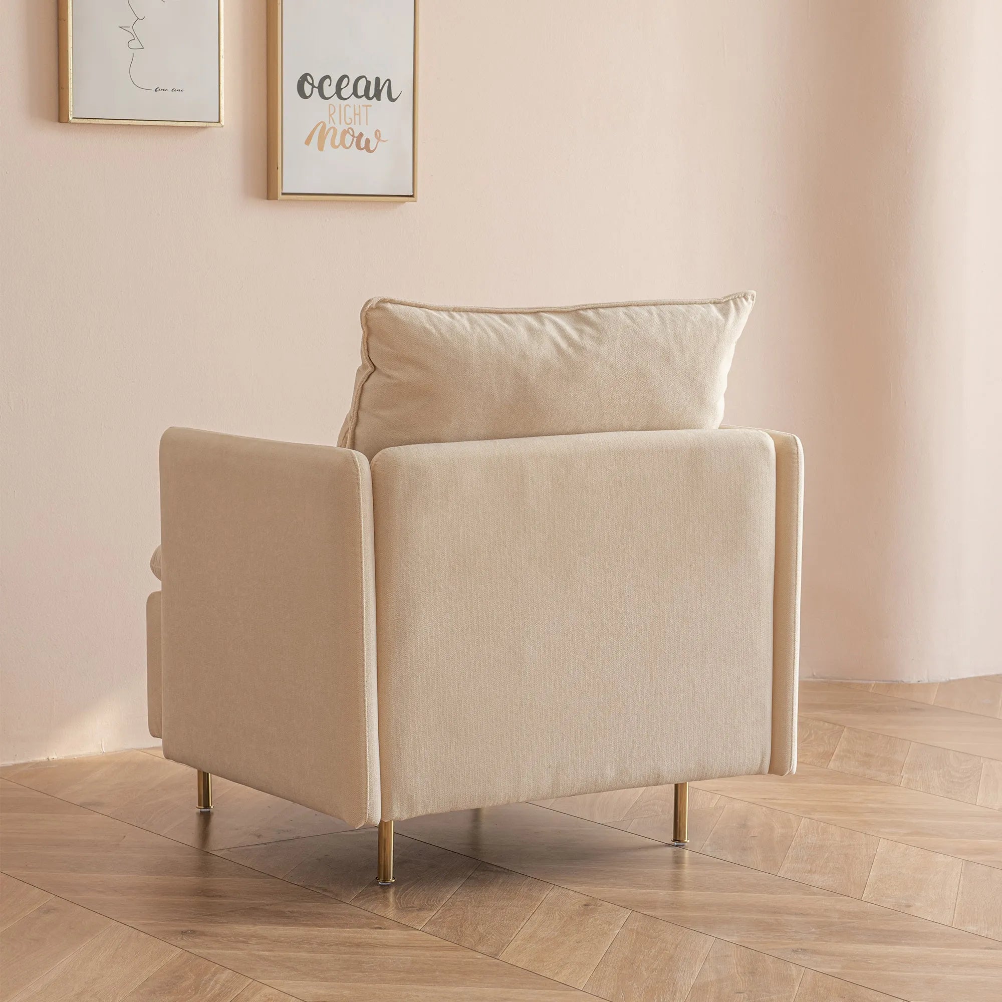 A beige House of Effy MINIMALIST ACCENT CHAIR with a cushioned backrest, positioned on a wooden floor beside a light pink wall adorned with framed art prints, embodies modern design and sturdy solid hardwood construction.