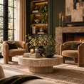 Load image into Gallery viewer, A styled living room scene with two tan upholstered barrel chairs are facing a round stone coffee table, set in front of a fireplace and built-in shelving. The room has dark green walls, a textured rug, candles, books, and greenery.
