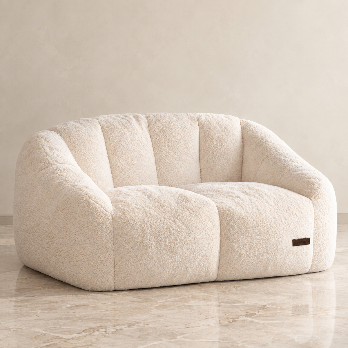 A cream-colored, plush boucle-style lounge chair with a curved back and wide armrests, set against a matching beige textured wall and marble floor.