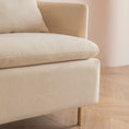 Load image into Gallery viewer, Close-up of a beige, upholstered MINIMALIST ACCENT CHAIR corner by House of Effy with a cushion, showcasing modern design with brass legs and a wooden floor in the background.
