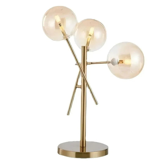 The House of Effy's GLASS BALL TABLE LAMP features a modern gold design with three asymmetrically arranged glass ball light bulbs on a circular base, creating an opulent glow and luxurious ambiance.