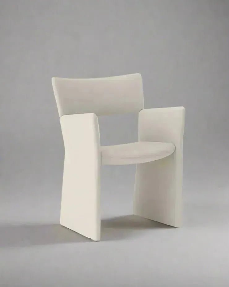 A luxurious, white CONTEMPORARY FABRIC DINING CHAIR by House of Effy with a curved backrest and wide armrests, embodying modern design and set against a plain gray background.