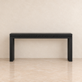 Load image into Gallery viewer, A black console table with a beaded nailhead trim along the front edge, set against a neutral beige textured wall and tiled floor.
