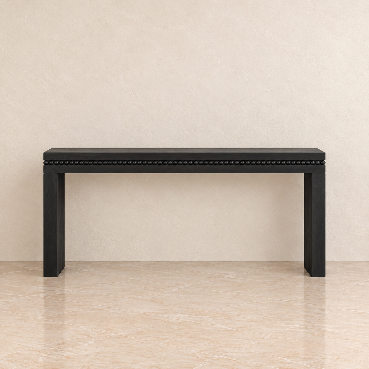 A black console table with a beaded nailhead trim along the front edge, set against a neutral beige textured wall and tiled floor.
