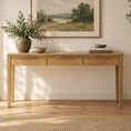 Load image into Gallery viewer, A light natural wood console table with three drawers and open legs, styled in a bright living room setting with a vase, books, and a framed landscape print.
