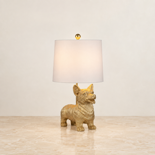 A table lamp featuring a textured gold dog figurine base and a white drum shade, set against a neutral beige background.