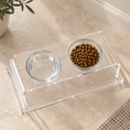 Load image into Gallery viewer, Clear acrylic pet feeder and water bowl tray holding two glass bowls, one with dry dog food and one empty, placed on a beige stone floor.
