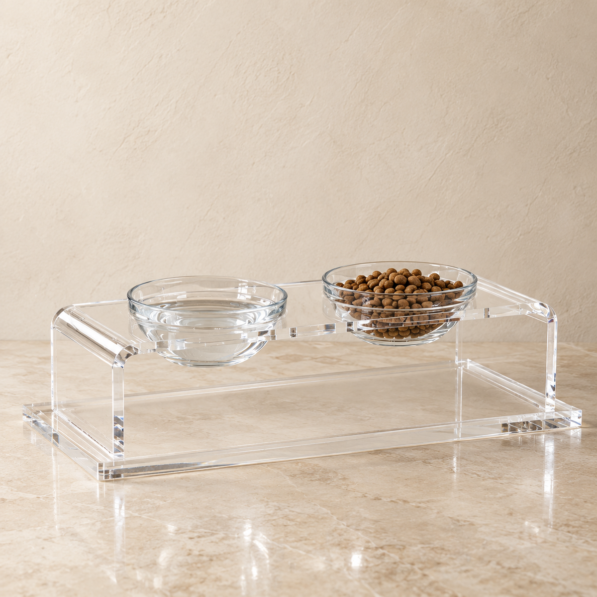 Clear acrylic double pet feeder and water bowl stand with two glass bowls, one filled with water and the other with kibble, on a beige marble surface against a textured beige wall.