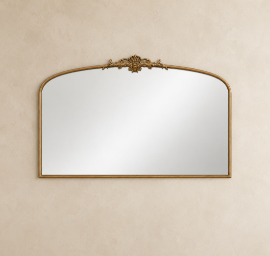 An ornate arched wall mirror with a gold-toned frame and decorative crest at the top, mounted on a textured beige wall.