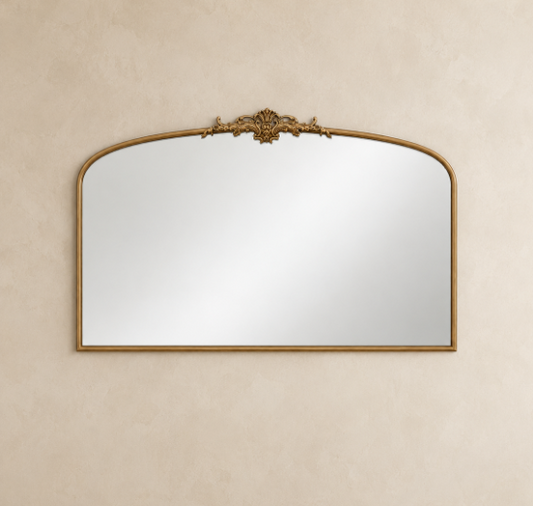 An ornate arched wall mirror with a gold-toned frame and decorative crest at the top, mounted on a textured beige wall.