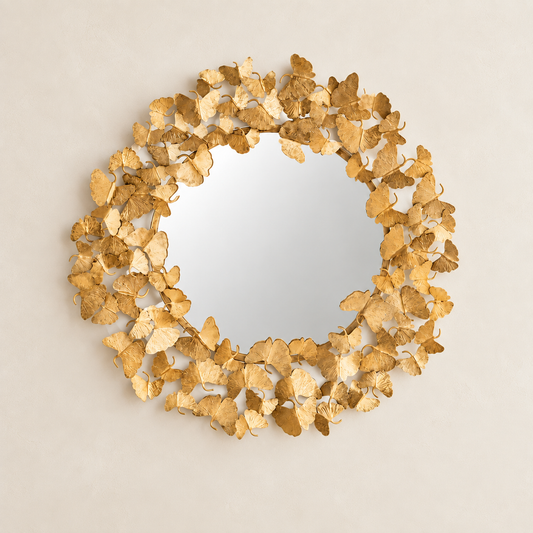 A round decorative mirror with a textured frame made of overlapping metallic gold leaf pieces, shown against a plain light beige background.