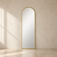 Load image into Gallery viewer, An arched full-length floor mirror with a slim gold frame, standing against a textured beige plaster wall on a light stone floor with soft window shadows.
