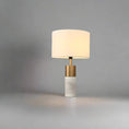 Load image into Gallery viewer, A House of Effy MODERN BEDSIDE LAMP with a cylindrical, marble-like base and a golden stem, topped with a white fabric lampshade, set against a plain grey background. This minimalistic design provides ambient lighting perfect for any contemporary bedroom.
