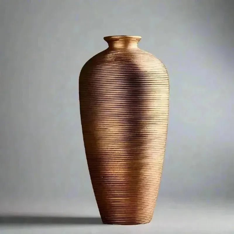 A BRONZE MODERN CERAMIC VASE from House of Effy, textured and copper-colored, sits elegantly on a smooth surface with blurred background elements including greenery and furniture. Ideal for enhancing your home decor with a contemporary touch.