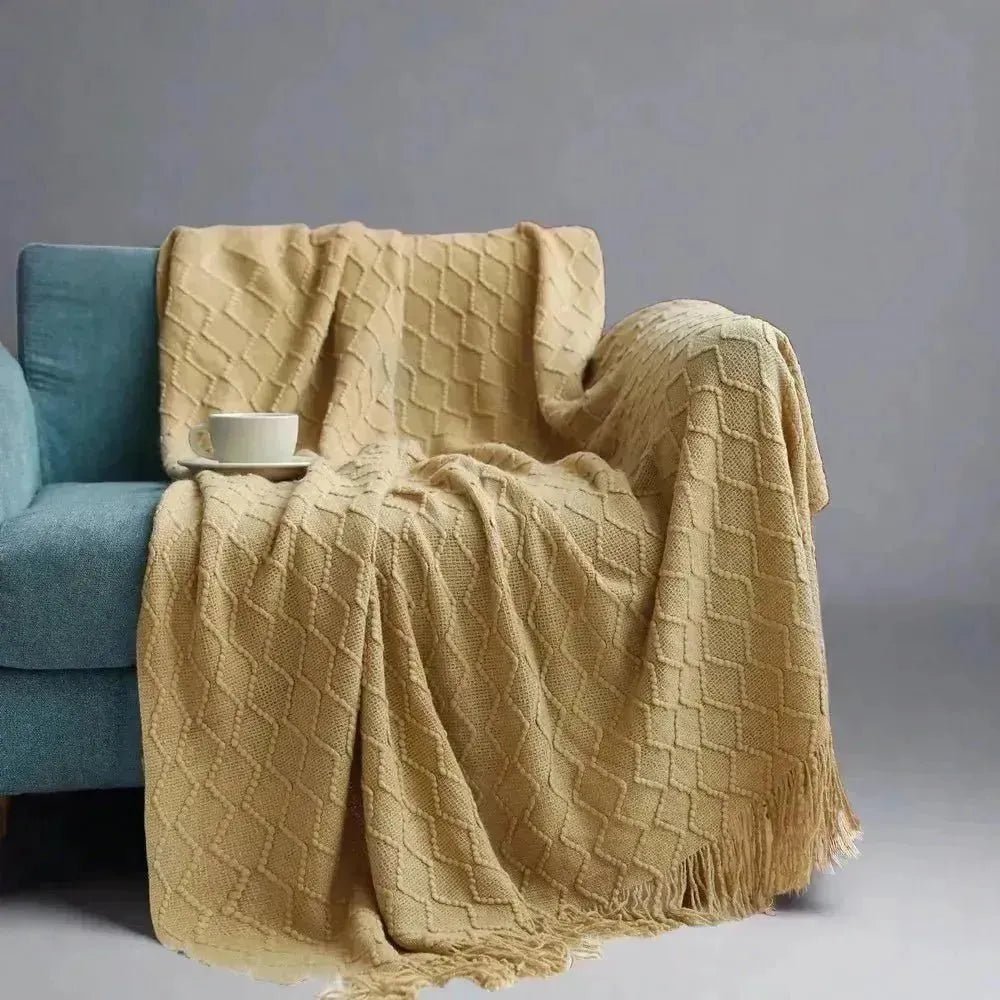 A beige textured solid knitted throw draped over a teal sofa with a white cup and saucer placed on the armrest. (House of Effy)